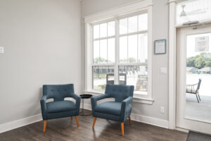 two blue chairs next to a window and door in the interior of the ellingsworth commons clubhouse